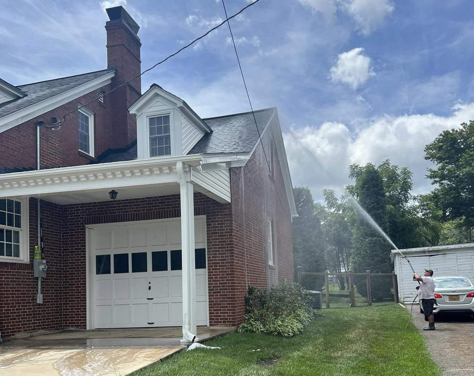 Washing a two story brick home from the ground, the spray reaching the roof line above the garage