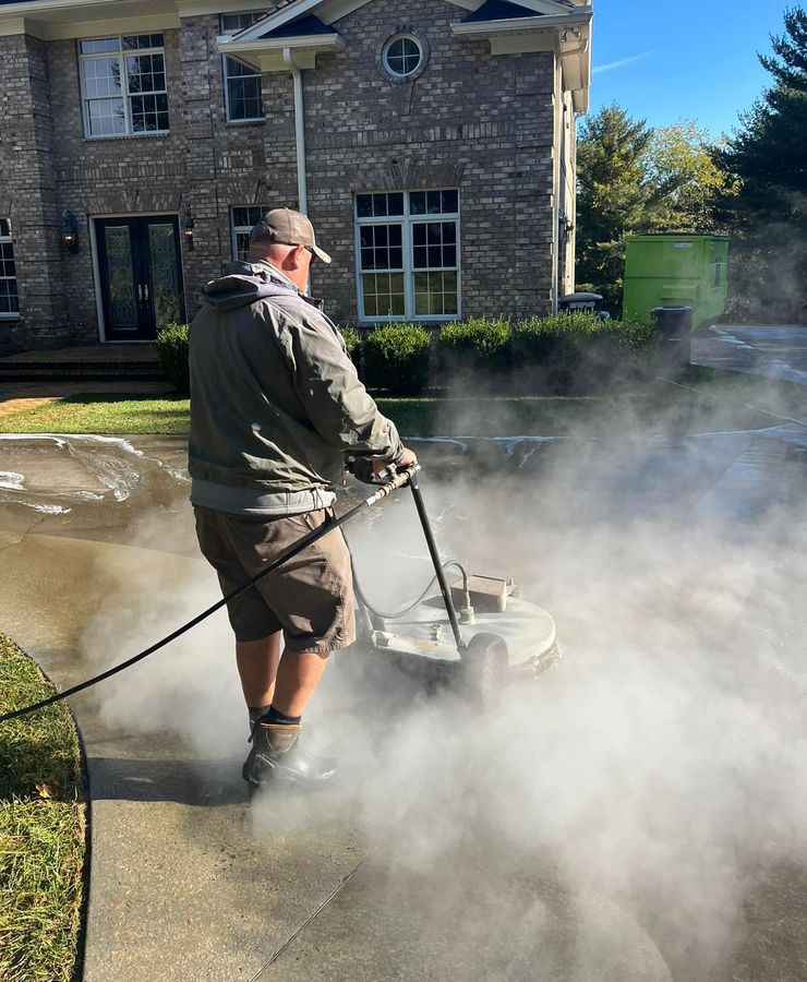 Surface cleaning a driveway beside a brick home, steam kicking up off the concrete